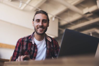 Modern dizüstü bilgisayarlı neşeli erkek metin yazarının portresi çalışma alanındaki masa başında poz veriyor, dijital netbook ile mutlu beyaz programcı serbest meslek sırasında kameraya gülümsüyor.