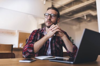 Optik gözlüklü düşünceli erkek programcı dizüstü bilgisayardaki veri pazarlama fikri üzerine kafa yoruyor, netbook 'lu düşünceli yazılım geliştiricisi başlangıç projeksiyonunda grafik tasarımı hakkında düşünüyor