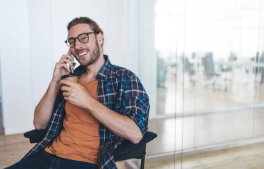 Zeki girişimci cep telefonu uygulamasını kullanarak kablosuz bağlantıyı kullanıyor, gözlüklü mutlu milenyum adamı kahve molası sırasında mobil konuşma ve iletişim kuruyor.
