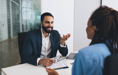 Ofisteki beyin fırtınası sırasında gülümseyen profesyonel patron ortağıyla iletişim kuruyor, masa başındaki meslektaşları pazarlama için iş toplantısından keyif alıyor.