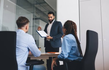 Resmi takım elbiseli kendine güvenen erkek direktör zeki meslektaşları ve Orta Doğulu işadamlarıyla birlikte raporları incelerken üretken strateji sunumu yapıyor.