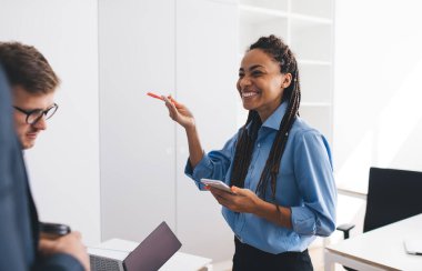 Modern mobil cihazlı mutlu Afrika kökenli Amerikalı kadın çalışanlar iş arkadaşlarıyla iletişim kuruyor. Ofis içi brifingde birlikte vakit geçiriyorlar. Cep telefonlu neşeli bir kadın iş görüşmesi yapıyor.