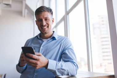 Boş zamanlarında kameraya gülümseyen dijital hücresel teknolojisi olan neşeli beyaz adamın yarım boy portresi. Modern mobil cihazıyla 30 'lu yaşlardaki mutlu erkek blogcu.