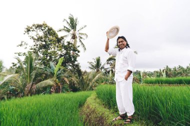 Endonezya 'daki iş plantasyonunda elinde şapkası olan mutlu bir çiftçinin portresi. Vietnam' da tatillerde çeltik tarlalarını ziyaret eden neşeli bir adam.