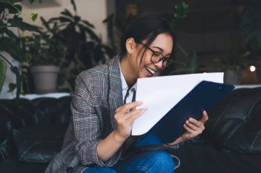 Görsel koruma için optik gözlük takan neşeli bayan girişimci. Evrak işlerini incelerken gülümsüyor. Klasik gözlüklü başarılı bir gazeteci.