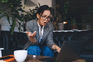 Şaşkın kadın metin yazarı klasik göz giysisi soling web sorunları modern netbook teknolojisi üzerinde taranmış yayınlar, gözlüklü ciddi Asyalı kadın dizüstü bilgisayardan gelen e-posta haberleriyle kafası karışmış