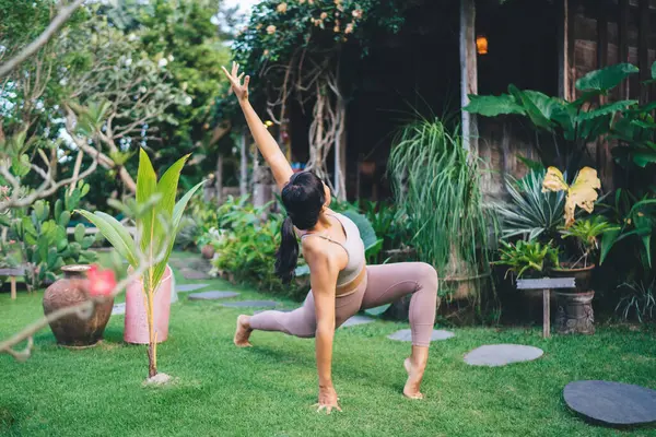 stock image Girl practicing yoga in Recolver side angle pose outdoor. Concept of healthy lifestyle. Young beautiful athletic woman wearing sportswear and barefoot on green grass in yard on Bali island. Daytime