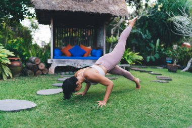 Bahçedeki yeşil çimlerde yoga yapan bir kız. Uyum ve akıl sağlığı kavramı. Bali adasında spor giyimli ve çıplak ayaklı çekici bir kadın. Gündüz
