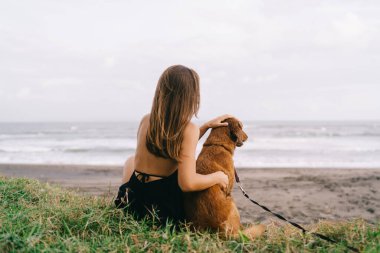 Köpekli bir kadının sahil şeridinde güzel vakit geçirmesi, genç bir bayanın tüylü köpek evcil hayvanıyla dinlenmesi yaz tatillerinde sakin sahil ziyaretlerinin keyfini çıkarması.