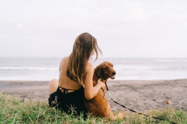 Köpekli bir kadının sahil şeridinde güzel vakit geçirmesi, genç bir bayanın tüylü köpek evcil hayvanıyla dinlenmesi yaz tatillerinde sakin sahil ziyaretlerinin keyfini çıkarması.