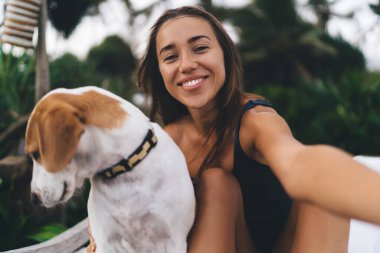 Mayo giymiş mutlu beyaz kadın portresi en sevdiği köpeğe sarılıyor. Haftasonu dinlenme odasında aşk duyguları hissediyor. Yakalı sevimli bir evcil hayvan olan neşeli hippi kız kameraya gülümsüyor.