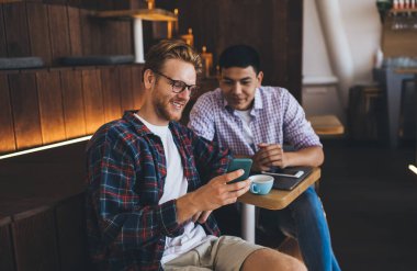 Genç çok ırklı ofis çalışanları akıllı telefondan bir şey izliyor. İş birliği ve takım çalışması kavramı. Modern başarılı adamlar. Birlikte çalışan Asyalı ve Kafkasyalı adamlar.