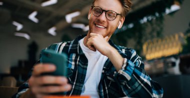 Beyaz adamın akıllı telefondan bir şey izlediği görüntüler. Uzaktan eğitim ve iş kavramı. Modern, başarılı bir adamın fikri. Gözlüklü genç adam geniş ofiste çalışıyor ya da çalışıyor.