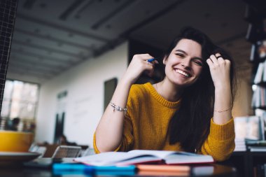Neşeli bir kız öğrencinin gün içinde rahat bir kafede otururken gülümseyip ödev yapması.