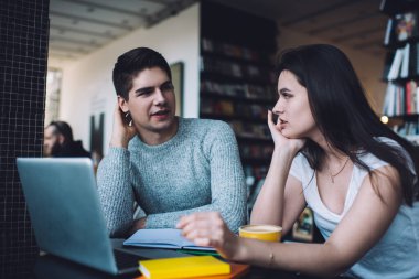 Odaklanmış genç adam ve kadın günlük kıyafetlerle birbirlerine bakıyorlar ve kafede iş görüşmeleri sırasında doküman ve laptopla sohbet ediyorlar.