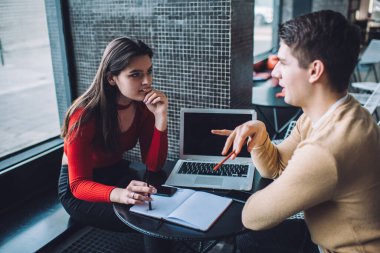 Pencere kenarında dizüstü bilgisayarla otururken ders çalışmanın sorunlarını tartışan meşgul erkek ve bayan üniversite öğrencilerinin yüksek açısı