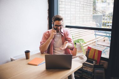 Uzaktan çalışan bir meslektaşla akıllı telefon görüşmesi yapan mutlu bir erkek serbest yazar, cep telefonuyla alışveriş yapan gülümseyen bir adam netbook bilgisayarından online alışveriş yapıyor.