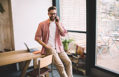 Optik gözlüklü gülümseyen hippi adam boş zamanlarında mobil uygulama kullanarak dijital akıllı telefon teknolojisiyle telefon etmek için 4G internete bağlanan neşeli bir erkek.