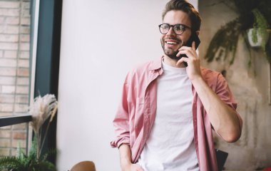Milenyum hipster 'ı optik göz giysisi giyen adam boş zamanlarında cep telefonu uygulamasını kullanarak dijital akıllı telefon teknolojisiyle telefon etmek için 4G internete bağlanan neşeli bir erkek.