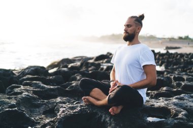 Kafkasyalı bir adam Asya 'da oturmuş yaşam enerjisi, rahatlık ve sükunet eğitimi alıyor. Nilüfer çiçeğinde meditasyon yapan sakin bir erkek kıyı şeridinde sağlık için yoga yapıyor.