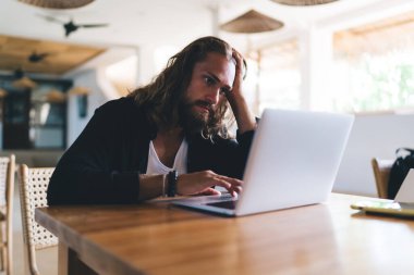 Yorgun erkek serbest çalışan, bilgisayardaki uygulamalar üzerinden kapalı mekanlarda 4G kablosuz ağ kullanarak internetten sohbet ediyor, hipster adam web sayfasına Netbook üzerinden bakınarak medya içeriğini indiriyor - uzaktan çalışıyor