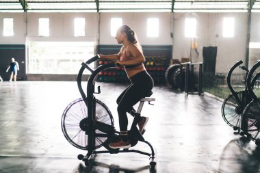 Eşofmanlı beyaz bir kadının spor malzemeleriyle spor yaparken spor yaparken spor yaparken, spor yaparken eğlenirken, spor yaparken spor yaparken, hayat dolu olduğu için vücut eğitimi sırasında bisiklet sürerken yan görünümü.