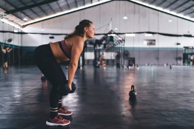 Aktif spor giyim sektöründe kararlı beyaz bir kadın spor aletleri kullanarak spor salonunda kardiyo eğitimi alıyor. Güçlü bir kadın halterleri ağırlık kaldırmada ve kas gücünü arttırmada kullanıyor.