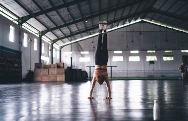 Spor salonundaki antrenman sırasında denge kuran bayan atletlerin arka planda duruşları, güçlü eşofman giymiş kadın amuda kalkıp enerji egzersizleri sırasında sağlıklı yaşam tarzını koruyor.