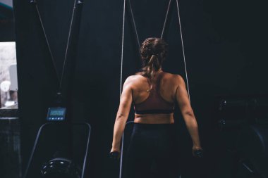 Vücut geliştirme alıştırması için spor stüdyosundaki spor simülatöründe egzersiz yapan kaslı bayan sporcuların arka plandaki görüntüsü.