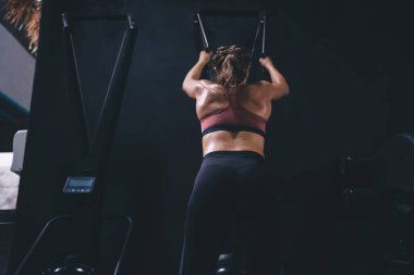 Profesyonel genç bayan atlet spor salonunun içinde çekiş makineleri üzerinde sıkı çalışıyor, formda bir kızın sağlıklı yaşam tarzını arka planda tutarken kapalı alanda ağırlık kaldırmak için simülatör kullanıyor.