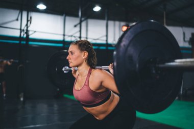 Eşofmanlı güçlü bir kadın ağır halter teçhizatıyla gol antrenmanı yapıyor. Kovalamaca dayanıklılığı, spor salonunda ağırlık kaldırma sporu yapan bir vücut geliştirme.