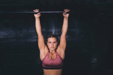 Vücut geliştirmede güçlü olan kadın vücut geliştirici egzersiz sırasında barfiks çekerken, beyaz kadın portresi tonusta atletik vücut şeklini korurken yatay barlarda enerjik ısınma sağlar.