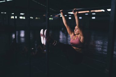 Güçlü atletlerin sportif kardiyo salonunda antrenman için yatay kolları olan zor bir sabah sporu var. Dayanıklılık egzersizi yaparken barfiks çeken kaslı genç bir kadın.