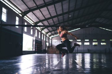 Sportif spor salonundaki kardiyo antrenmanı sırasında sert atlayan kararlı bayan sporcunun yan görüntüsü. Etkin giyimli kadın, formda kalmak için zayıflama yapıyor.