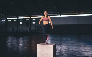 Sportif spor salonunda atlama egzersizi yapan genç ve zıpzıp kadın sporcu, kardiyo antrenmanı ve fiziksel dinlenme sırasında ince eşofman giyen beyaz kadın sporcu.