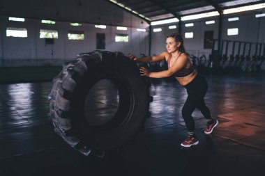 Kaslı vücutlu genç beyaz kadın ısınmak için ağır lastik teçhizatı kullanıyor ve halterci, spor formundaki kız formunu ve sağlıklı yaşam tarzını korumak için aktif egzersiz yapıyor.