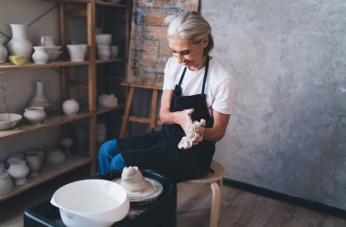 Gülümseyen Kafkas kadın üstat sanat stüdyosundaki çömlek çarkına kil tenceresi kalıbı döktükten sonra bez parçasıyla ellerini siliyor. Küçük işletmeler ve girişimcilik. Ev hobisi ve boş zaman. Kadınlar iş önlüğü giyer.