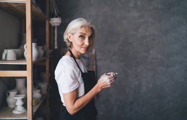 Beyaz kadın heykeltıraşın tahta sopayla seramik çömlek yapıp kameraya baktığı yan görüntü. Küçük işletmeler ve girişimcilik. Ev hobisi, eğlence ve eğlence. Sanat stüdyosu