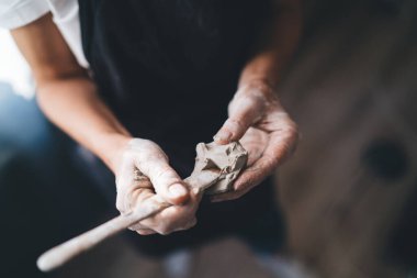 Sanat stüdyosunda olgun kadın pervazlarının seramik çömlekleri ahşap aletlerle kapladığı görüntüler. Küçük işletmeler ve girişimcilik. Ev hobisi, eğlence ve eğlence. İş önlüğü giyen kadın.