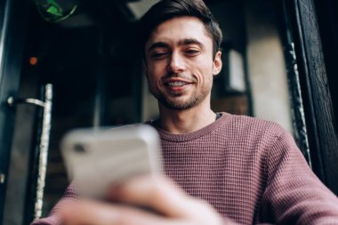 Boş zamanlarında mobil iletişimden keyif alan mutlu beyaz blogcu içerik metnini taramak için 4g kablosuz ağ kullanıyor, cep telefonu teknolojisi ile mesajlaşırken e-postaları kontrol eden gülümseyen hippi adam