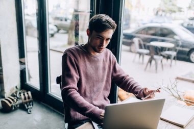 Modern dizüstü bilgisayar teknolojisi ve cep telefonu paylaşım medya dosyalarında birlikte çalışma alanındaki bluetooth bağlantısını kullanan beyaz yetenekli programcı, mobil ve netbook ağları olan genç hipster adam.
