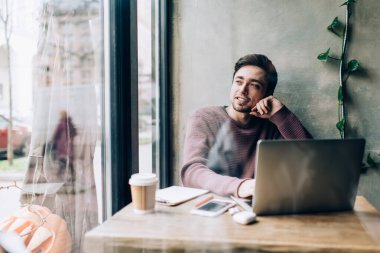 Düşünceli erkek öğrenci, modern dizüstü bilgisayar ve kahveyle birlikte çalışarak eğitim planını düşünmeyi öğreniyor. Netbook 'a özenli bakan yetenekli hippi çocuk.
