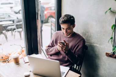 Modern dizüstü bilgisayar teknolojisi ve cep telefonu paylaşım medya dosyalarında birlikte çalışma alanındaki bluetooth bağlantısını kullanan beyaz yetenekli programcı, mobil ve netbook ağları olan genç hipster adam.