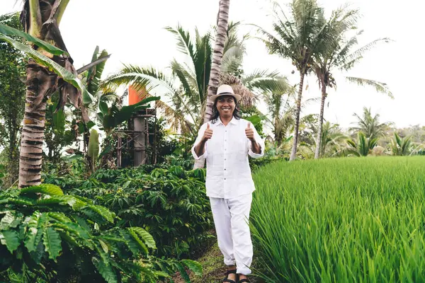 Gündüz vakti pirinç tarlalarında kahve çalısı ve kafein tohumu yetiştirmek için güler yüzlü beyaz elbiseli neşeli erkek çiftçi. Tarım işlerinden hoşlanan neşeli Balili adam.
