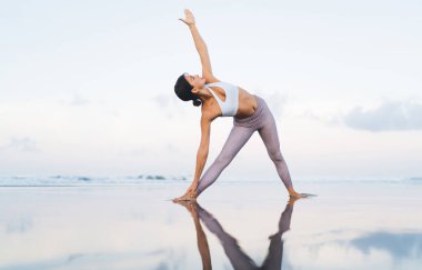Spor giyimli enerjik zinde bir kız Hatha yoga eğitimi sırasında meditasyon yapmak için sahilde sabahları eğleniyor, Asana 'da duran çekici bir kadın ve zindeliğe ulaşmak için mantralar deniyor.