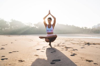 namaste 'de beyaz bir kadın, Asya' da denge kuruyor. Güneşli sahil şeridinde bacağını kaldırıyor. Sakin bir kadın, formda ve sağlıklı bir yaşam sürüyor.