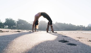Deniz kenarında sabah güneşinde hatha egzersizi yapan esnek kadın yogi. İnce vücut kaslarını esneterek kıyı şeridindeki pilates eğitiminde doğadan ilham alan sağlıklı kız.