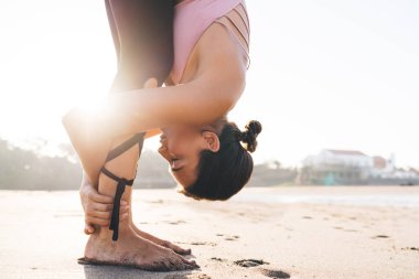 Kafkas kadın Yogi 'nin sabah kıyı şeridinde vücut ısısı esnerken yan görüntüsü. Eşofmanlı genç bir kadın vücut pozitifliğine ulaşmak için Asana' da sağlıklı yaşam tarzının tadını çıkarıyor.