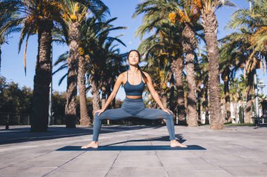 Sabah pilates yaparken vücut kaslarını esneten, kentteki caddede egzersiz yapan, Asyalı bayan yogi, paspas kullanarak geri çekilme eğitiminde sağlıklı yaşam tarzını koruyor.