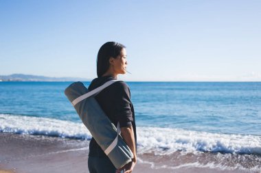 Spor giyim sektöründe spor yapan genç bir bayan antrenör deniz ufkuna bakarken hafta sonu kıyı şeridi antrenmanı için yer seçiyor. Çantalı çekici Asyalı kadın sağlıklı yaşam tarzını ve vücut pozitifliğini düşünüyor.